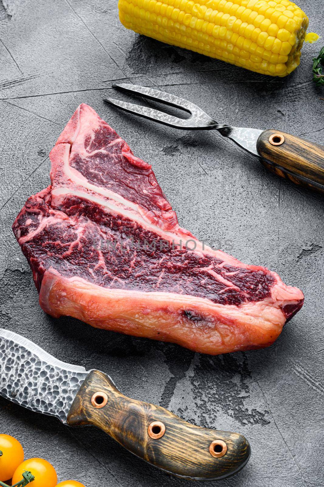 Cooking meat background. Raw aged beef t-bone steak, with spices and herbs for grill set, on gray stone background