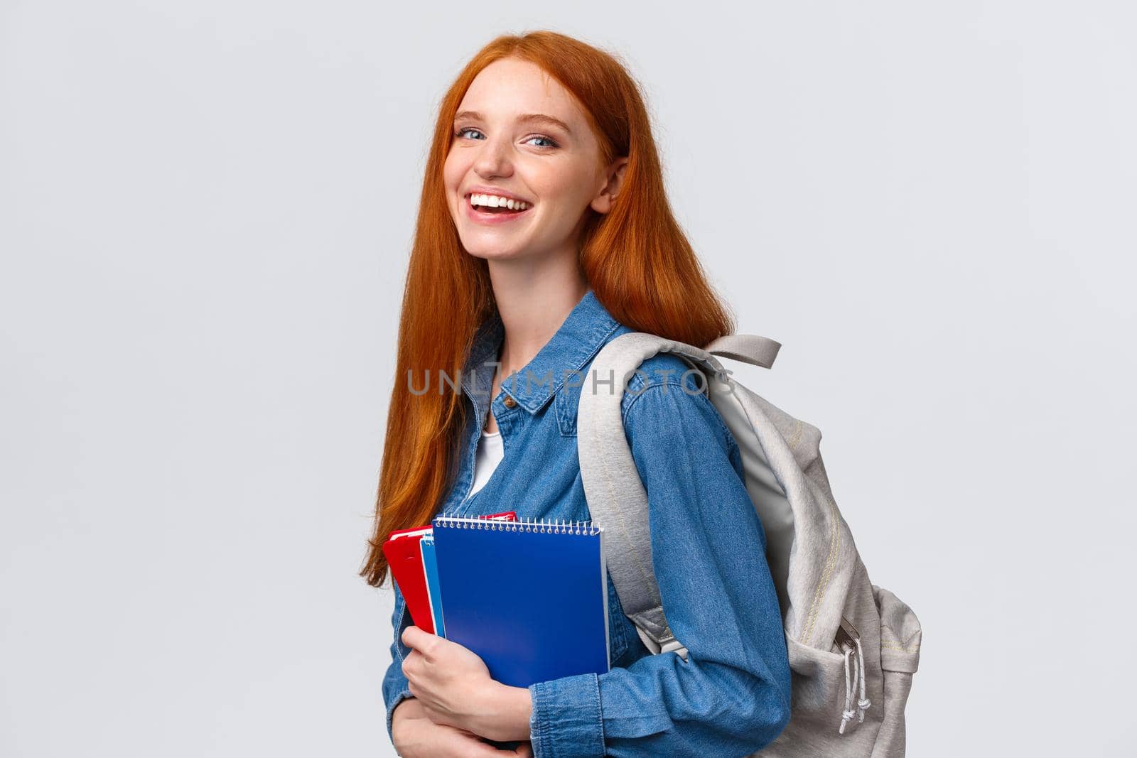 Students, education and studying concept. Lovely charismatic redhead foxy girl with backpack, notebooks and study books, standing white background, smiling joyful looking camera.