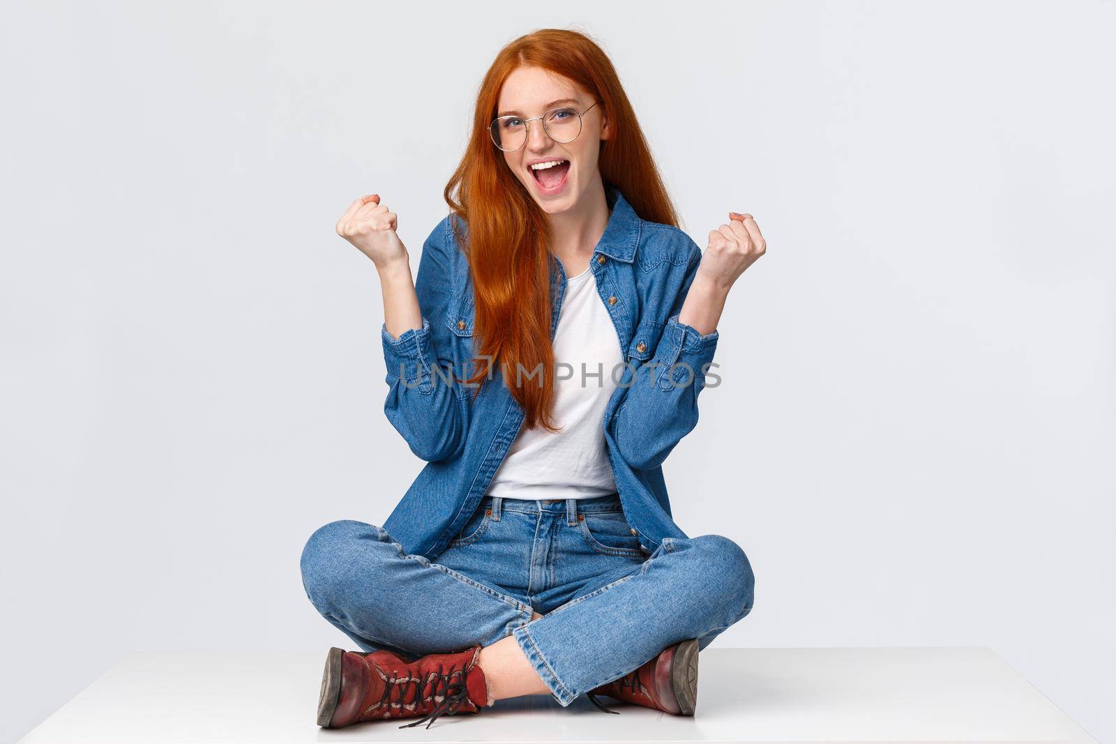 Cute and confident sassy redhead girl won challenge, sit floor, fist pump saying yes celebrating great news, winning competition, posing over white background satisfied, triumphing over achievement.