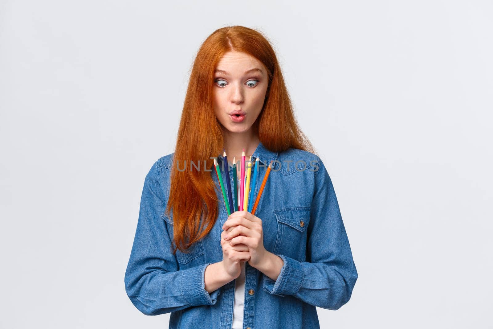 Girl eager start new art course, learn how to design, make models, standing with colored pencils, folding lips amused, looking at tools wondered and thrilled, drawing over white background.