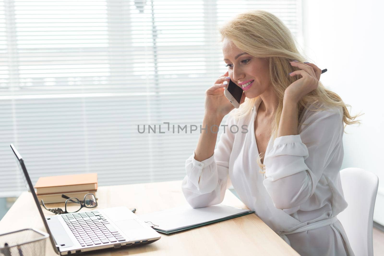 Business, technology and communication concept - blonde woman talking phone while watching laptop by Satura86