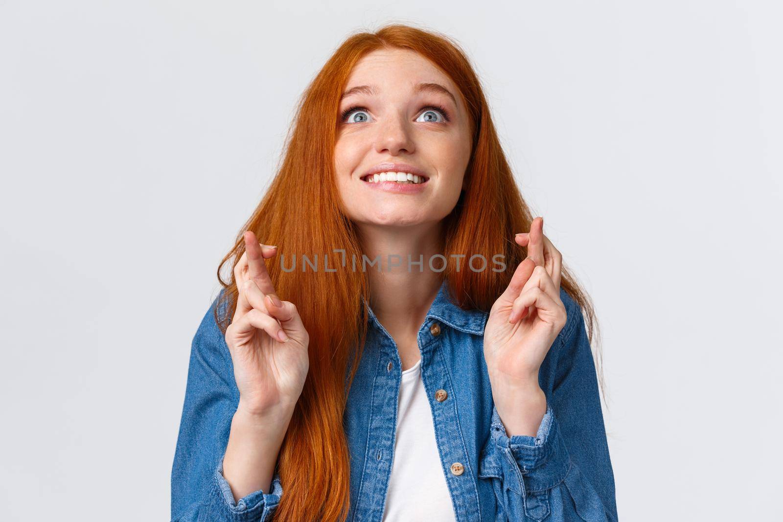 Excited and hopeful, optimistic cute redhead girl want dream come true, desire something, aspire achieve success good results, smiling looking up sky and making wish with fingers crossed good luck.