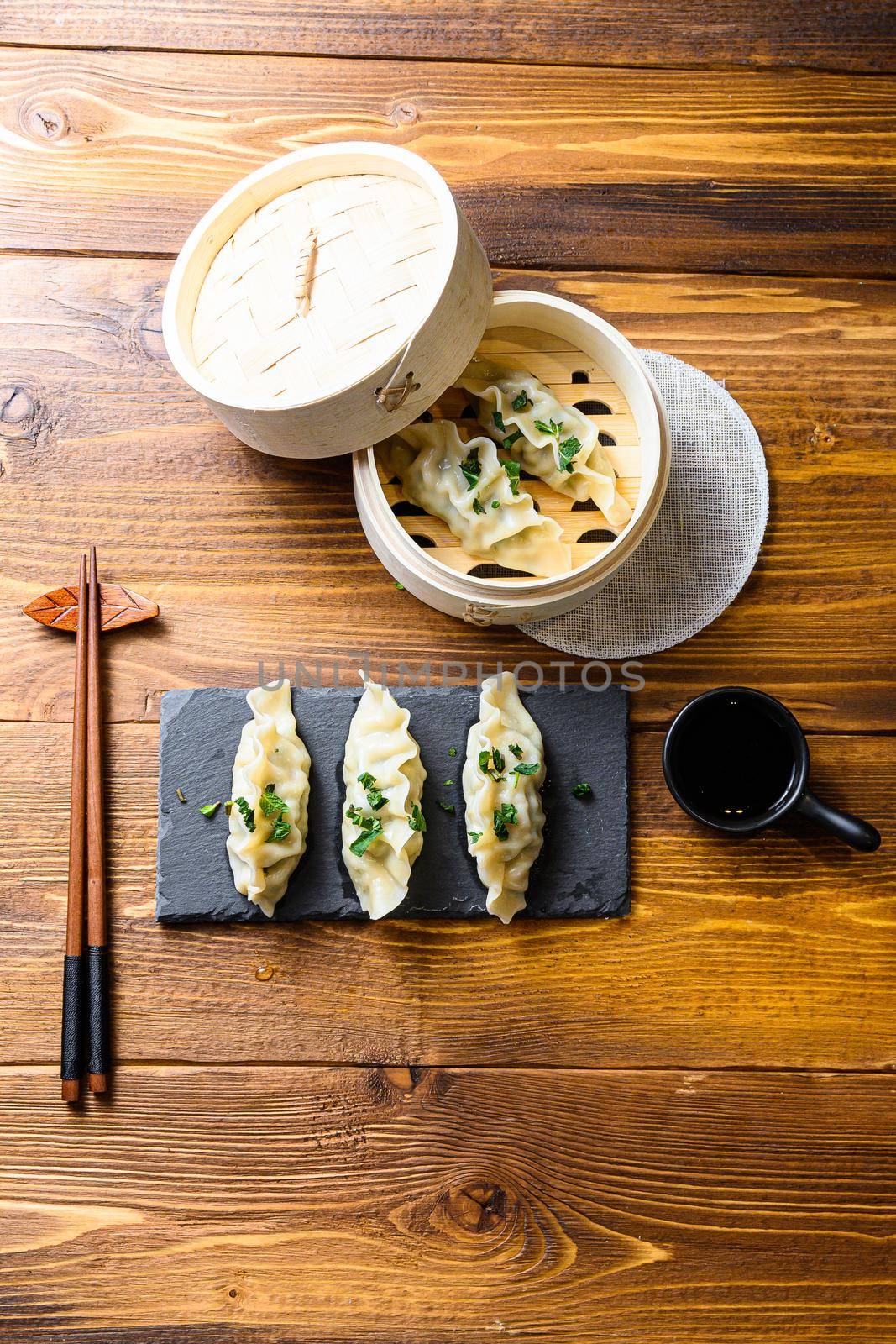 Top view fresh dumplings with wooden steamer on stone black slate. Chinese food on rustic old vintage wooden background. by Ilianesolenyi