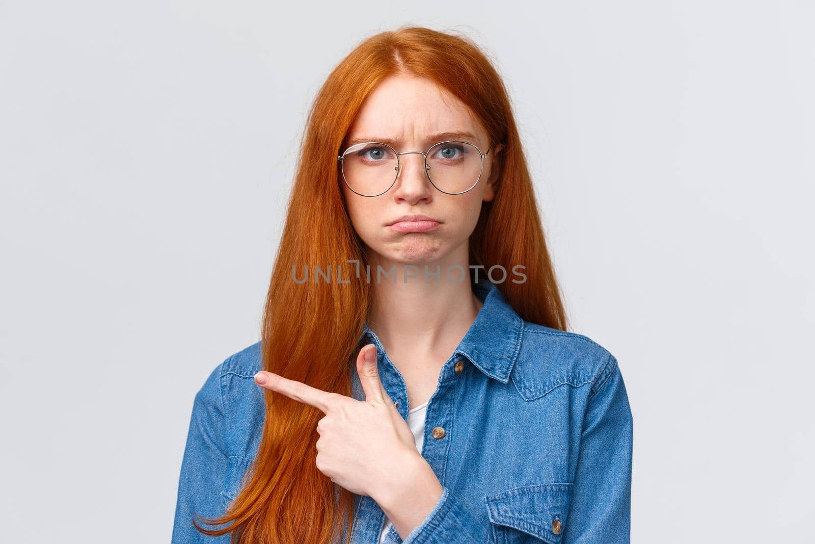 Close-up gloomy and upset, offended sulking girlfriend want something and pointing envy left, indicate disappointing promo, unfair situation, pouting and frowning look displeased, white background.