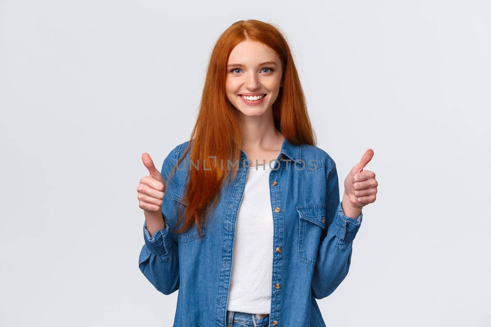 Waist-up portrait alluring confident smiling redhead female blogger review awesome new product, showing thumbs-up in approval, like or agree gesture, standing white background.