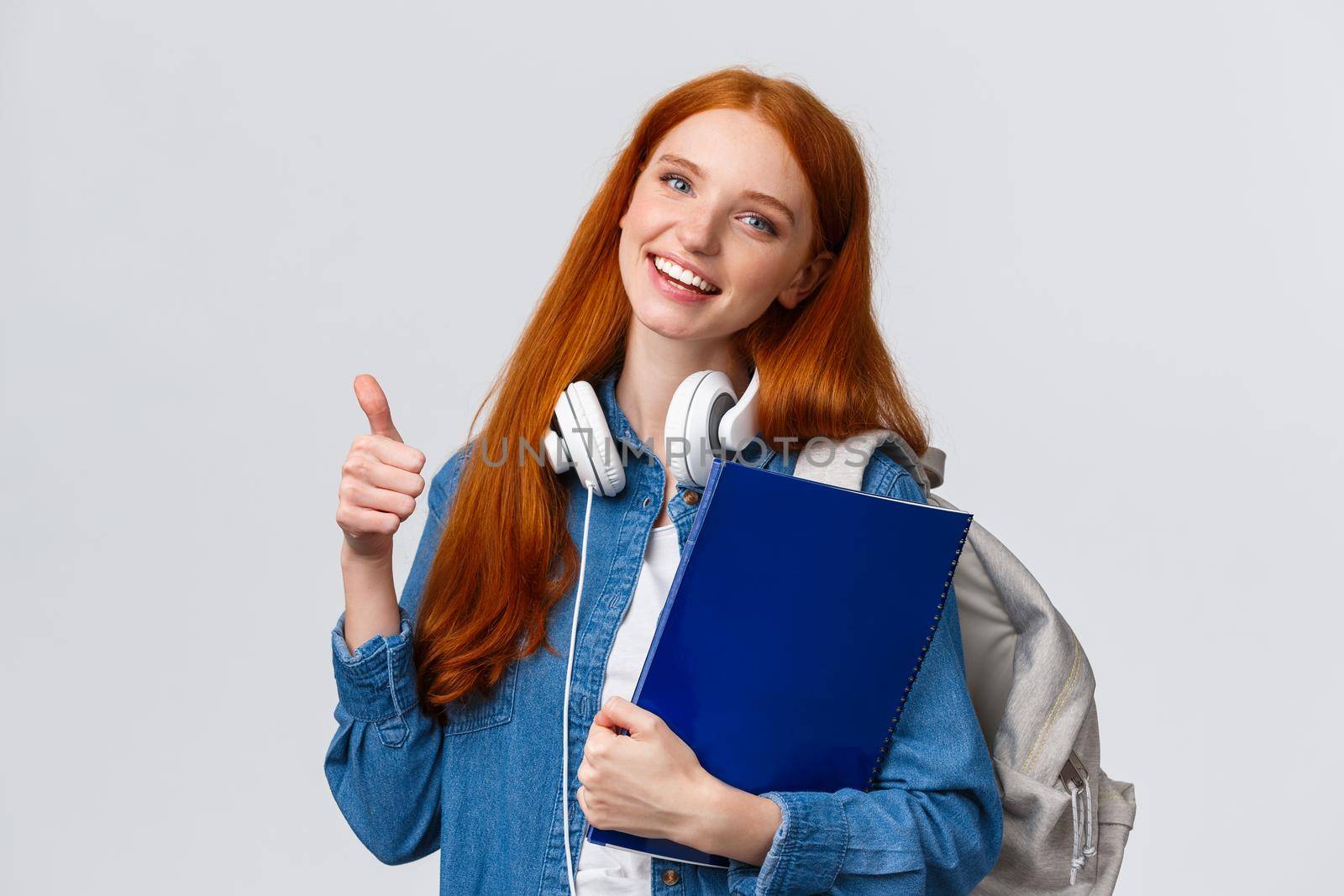 Education, teenagers and student lifestyle concept. Cheerful redhead lovely girl with backpack and folder, bring her portfolio to art, design class, showing thumb-up in approval, like gesture.