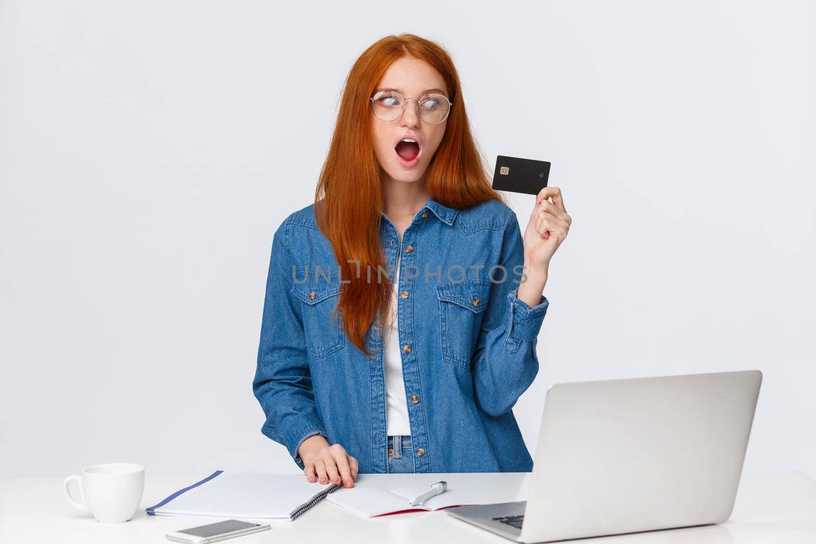 Shopaholic excited buy new things online. Thrilled and shook good-looking redhead female holding credit card look amused and astonished, standing near laptop, shopping internet.