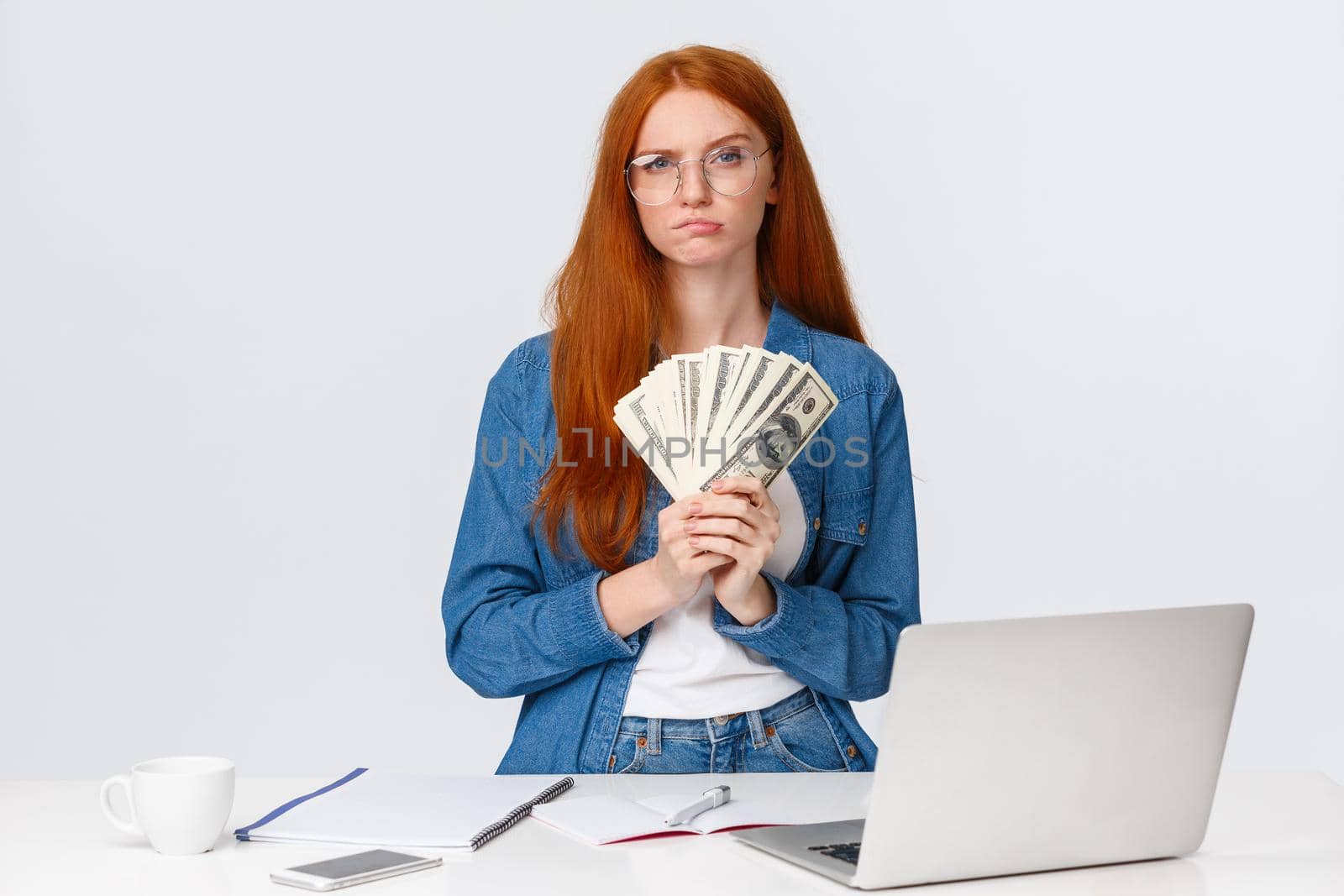 Thoughtful and hesitant serious-looking redhead female got payed, won big money prize in online art competition, freelancer recive payment and think how waste money, ponder over white background.
