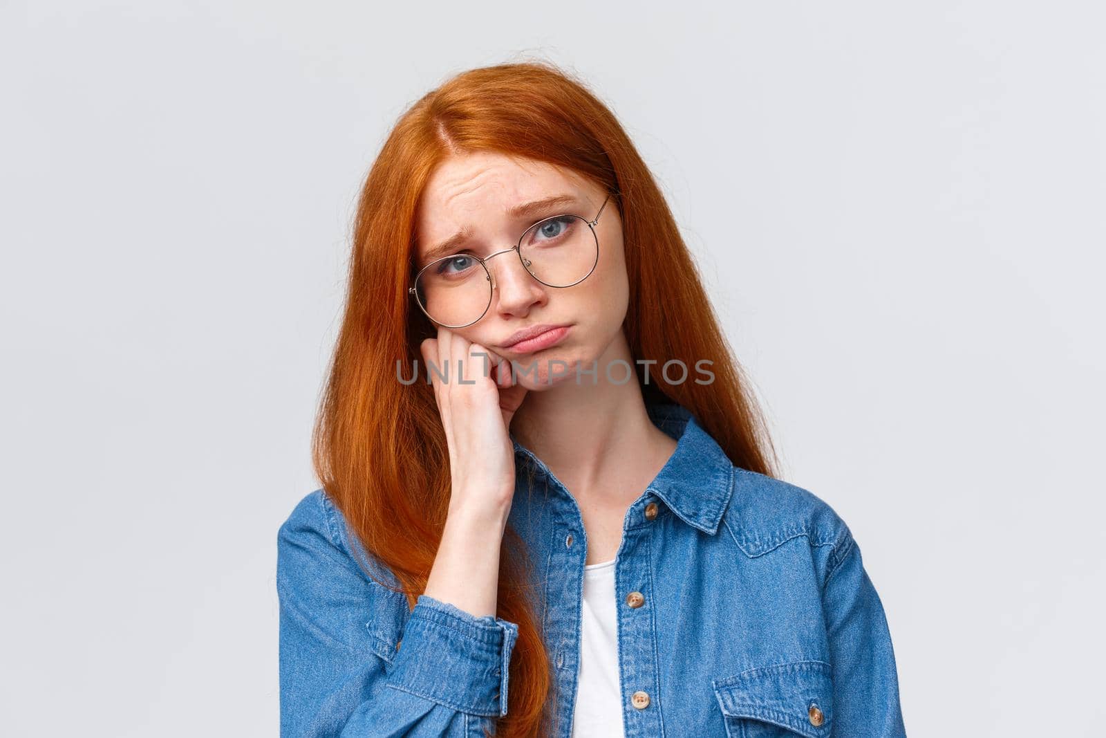 Close-up portrait gloomy unhappy redhead sad girl in glasses, teenager having bad day at college, leaning on hand pouting and sobbing, feeling hurt and distressed, standing depressed white background.
