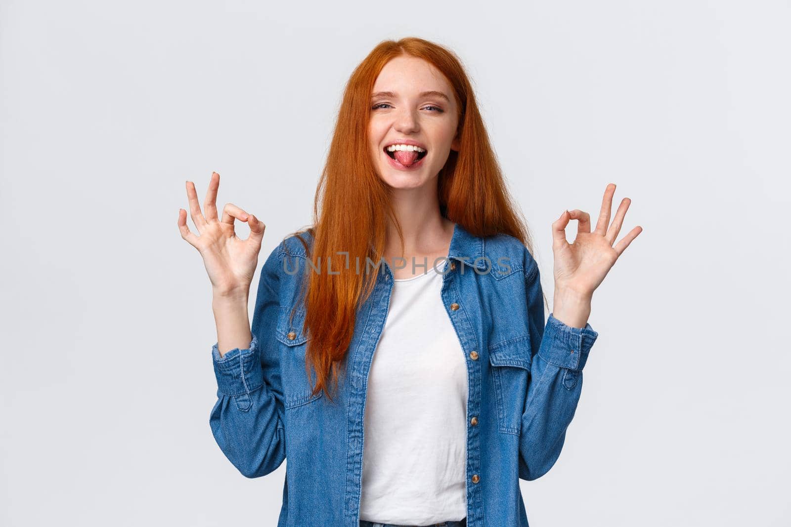 Relaxed and carefree, positive redhead girl chilling on party, having fun leisure weekends, showing okay gestures calming down, assuring all good, showing tongue and smiling playful.