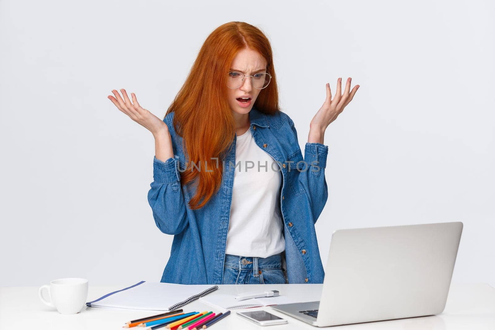 Mad and confused, frustrated redhead girl having troubles with computer, working on hard project, raising hands up dismay and annoyance, shrugging, stare laptop screen bothered.