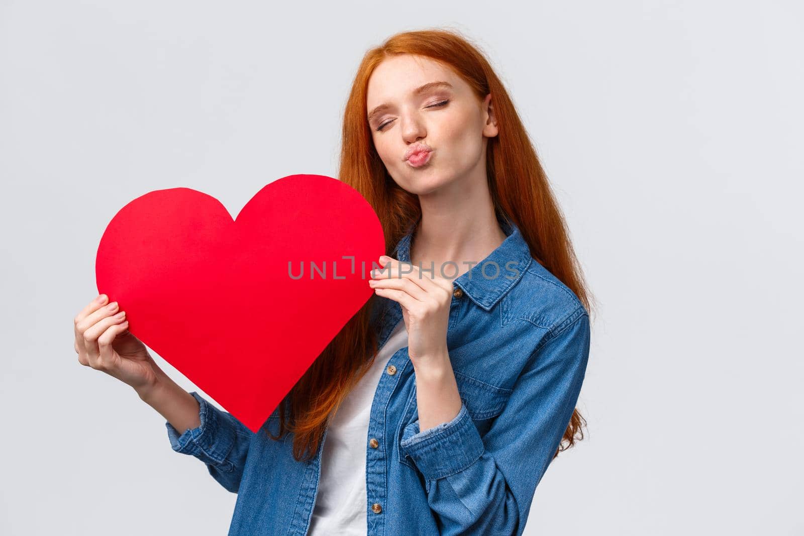 Romantic dreamy cute redhead teenager dreaming about giving boyfriend big red heart card to show her affection and love, celebrating valentines day with loved partner, standing white background.