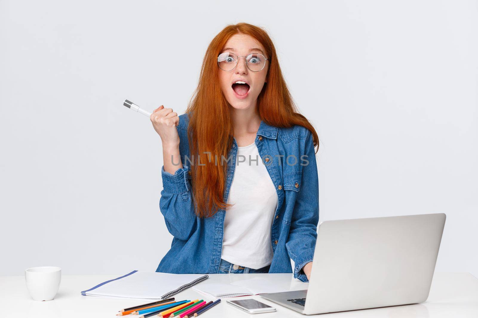 Amused, excited and surprised cute redhead girl telling roommate awesome news, read online great event nearby, smiling scream fascinated, standing near laptop and table with colored pencils.