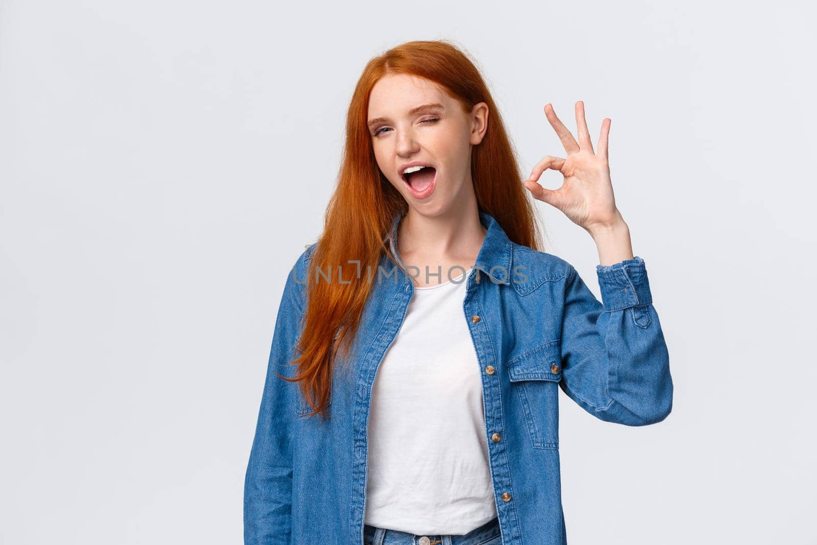 Waist-up portrait cheeky, confident and relaxed, chill redhead woman saying all alright, encourage everything okay, showing ok gesture wink and tongue, standing white background.