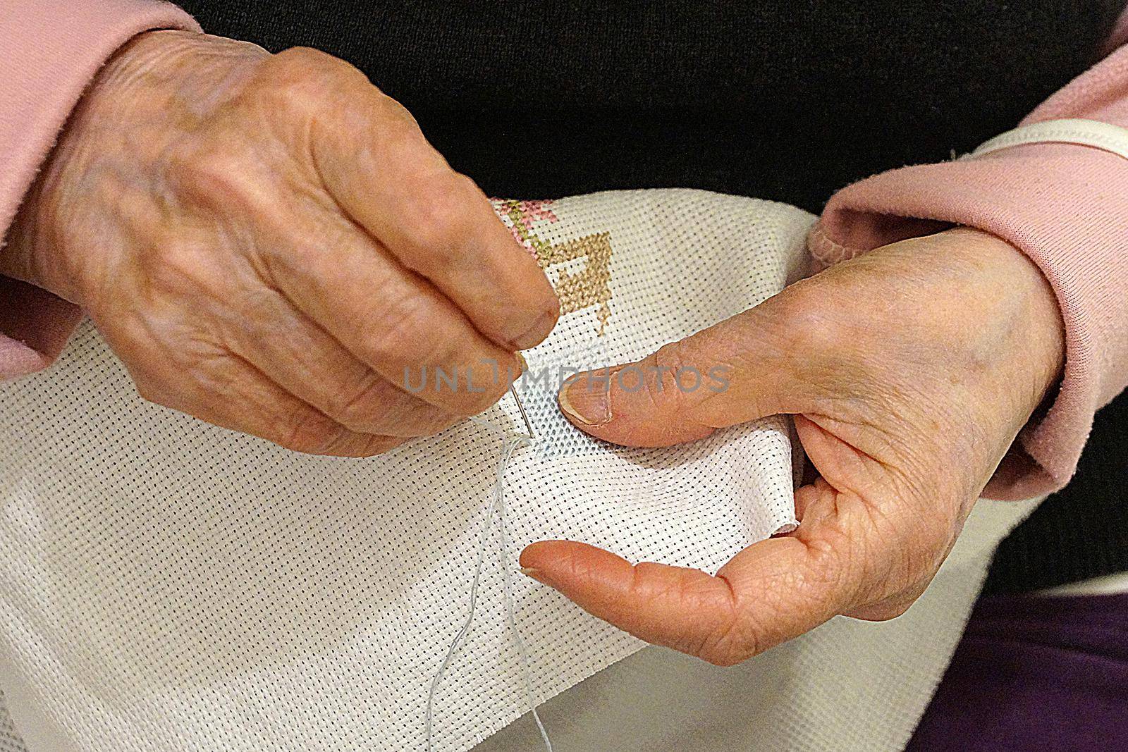 an elderly woman is embroidering a cross-stitch picture, hands close-up by Annado