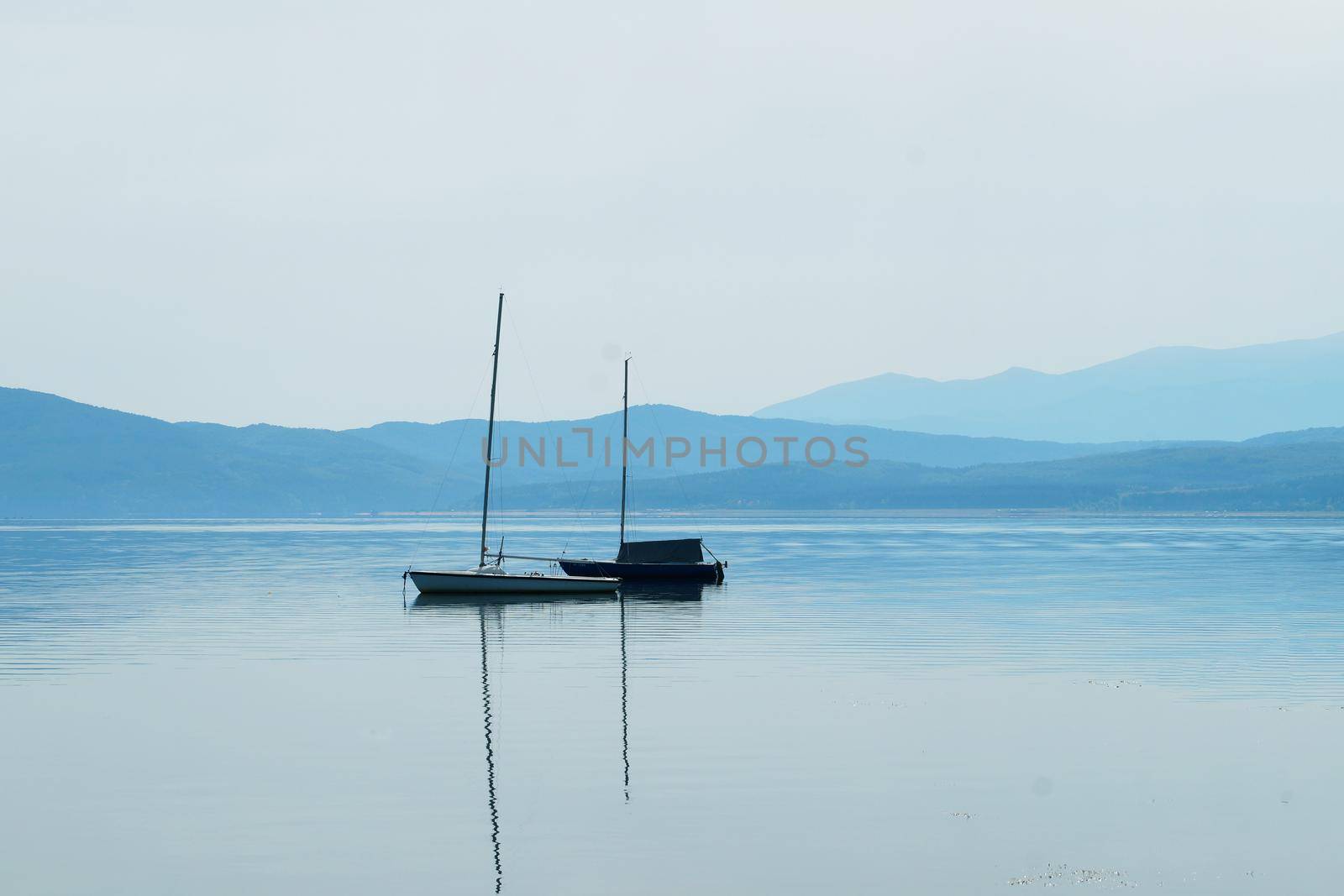 boat with masts on the water surface against the background of mountains in blue tones.