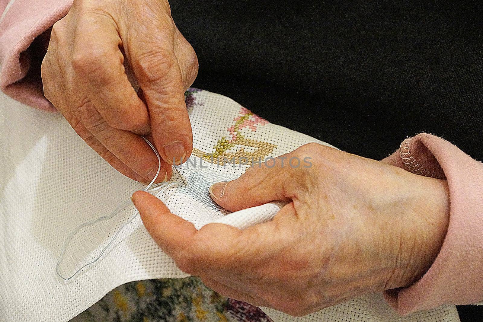 an elderly woman is embroidering a cross-stitch picture, hands close-up by Annado