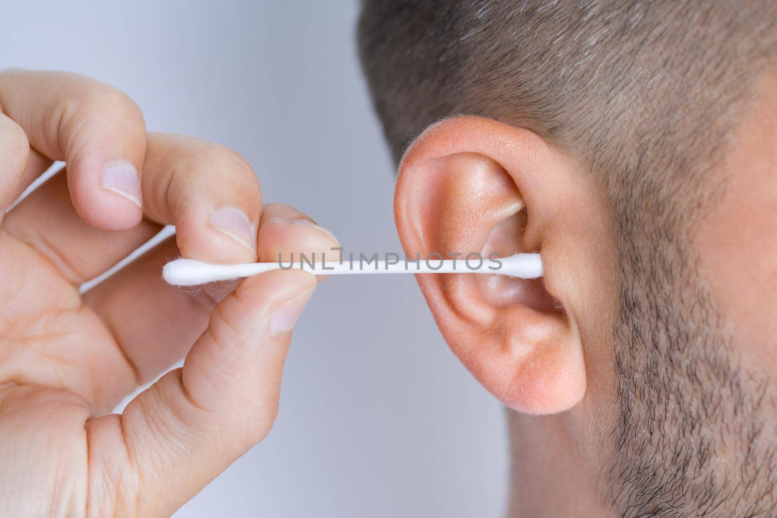 Closeup of man cleaning dirty ears with cotton swab or cotton stick. Ear cleaning and ear care. High quality photo