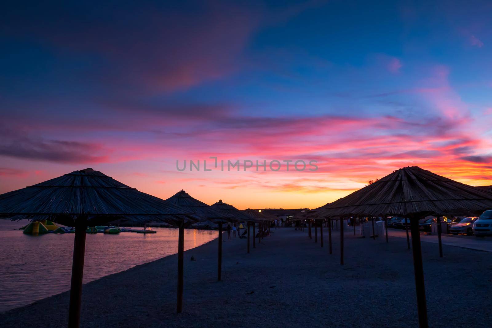 View of the beautiful blue and purple sunset, sky and straw beach umbrellas by zebra