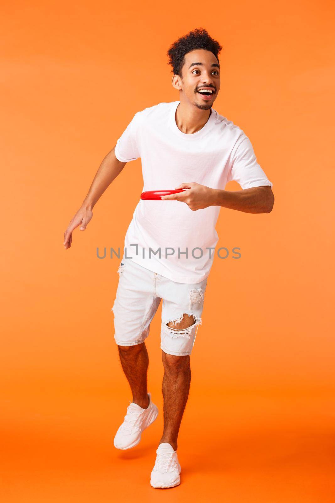 Full-length vertical shot happy, charismatic african-american sporty guy like active games outdoors, throwing frisbee at friend and smiling, enjoying beautiful sunny summer day, orange background.
