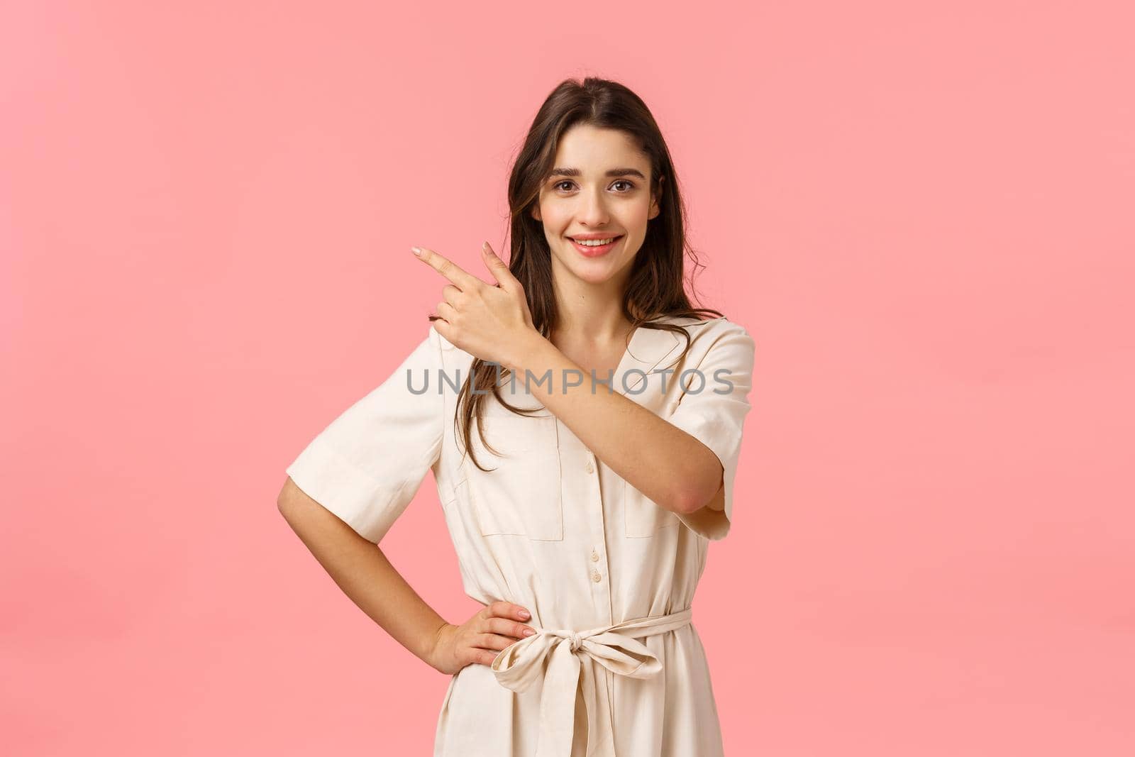 Optimistic gorgeous brunette caucasian female shoppaholic, pointing upper left corner and smiling assertive with enthuiastic positive grin, standing pink background joyful.