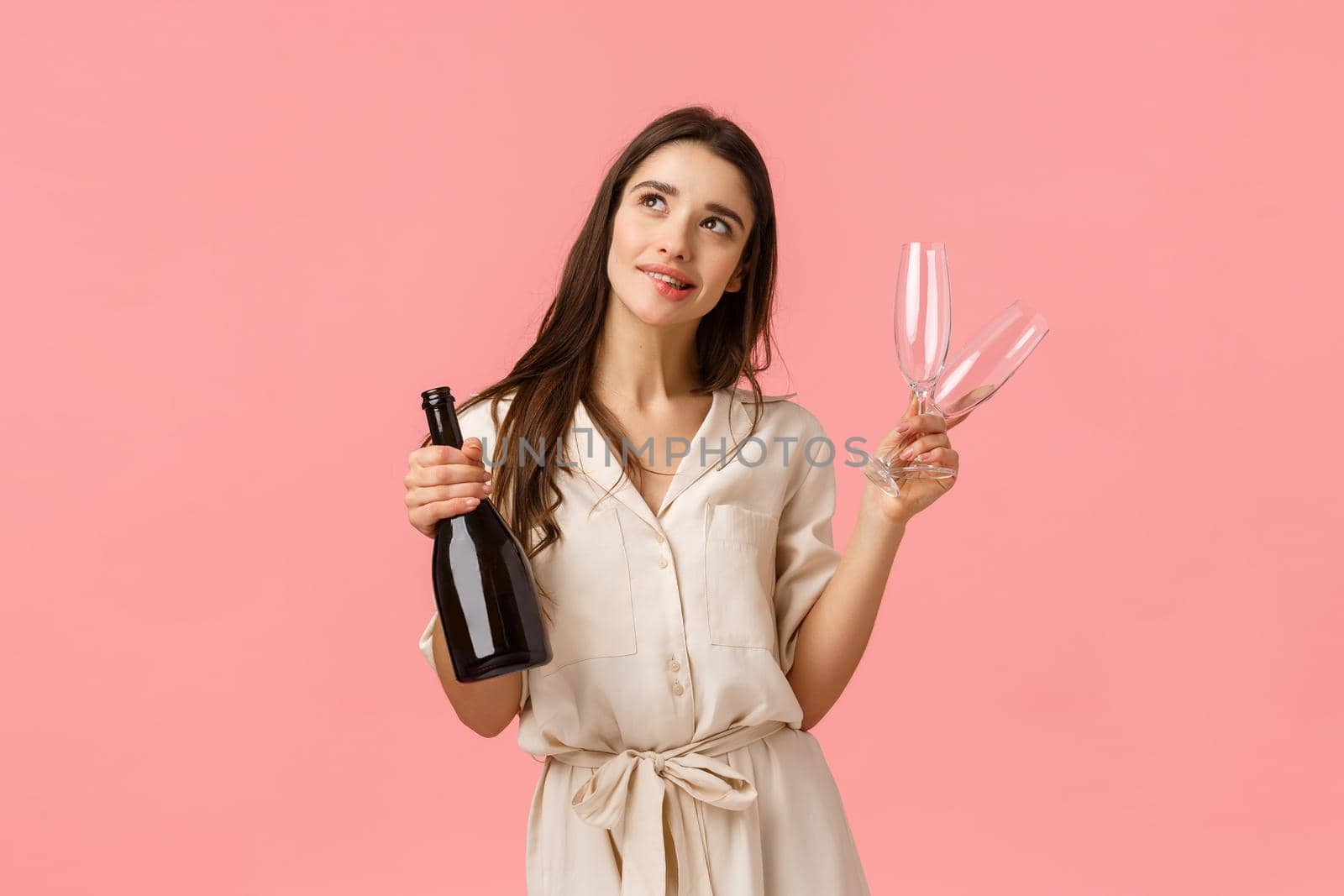 Dreamy and romantic young beautiful woman planning valentines day date, standing thoughtful looking up imaging perfect wedding, holding champagne and two glasses, smiling sensual.