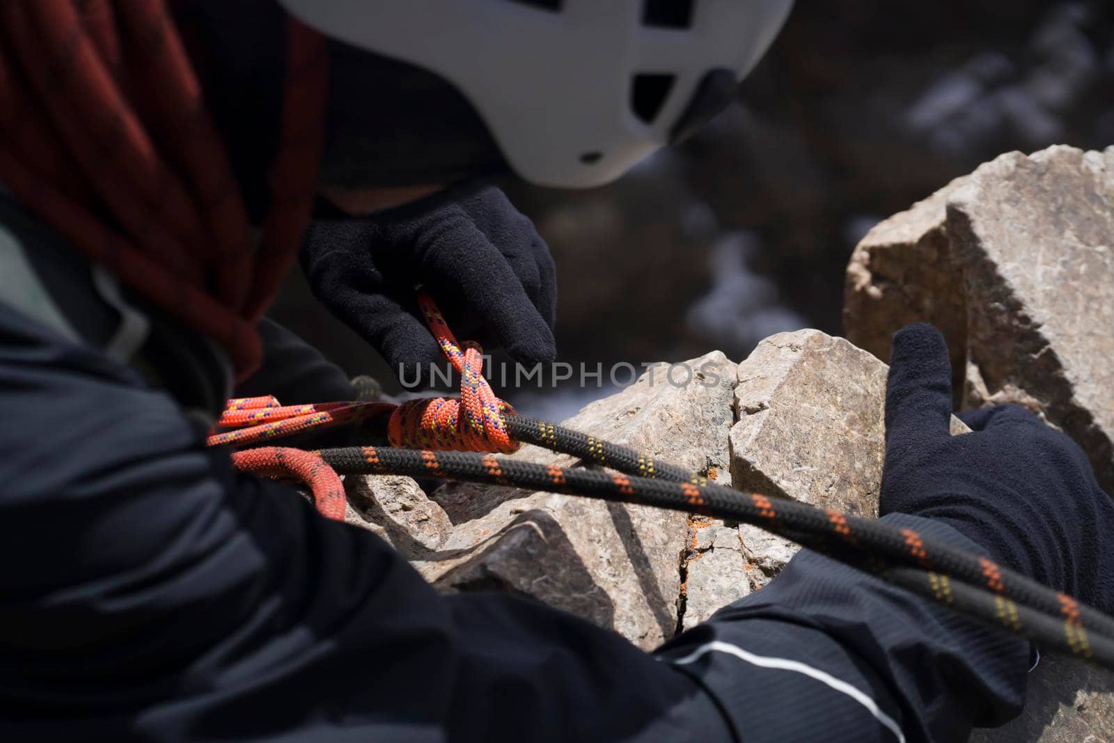 A young man in a helmet and with climbing equipment descends from the top of the mountain on a rope, the climber rappels with aperture-style self-braking belay in the snowy mountains.