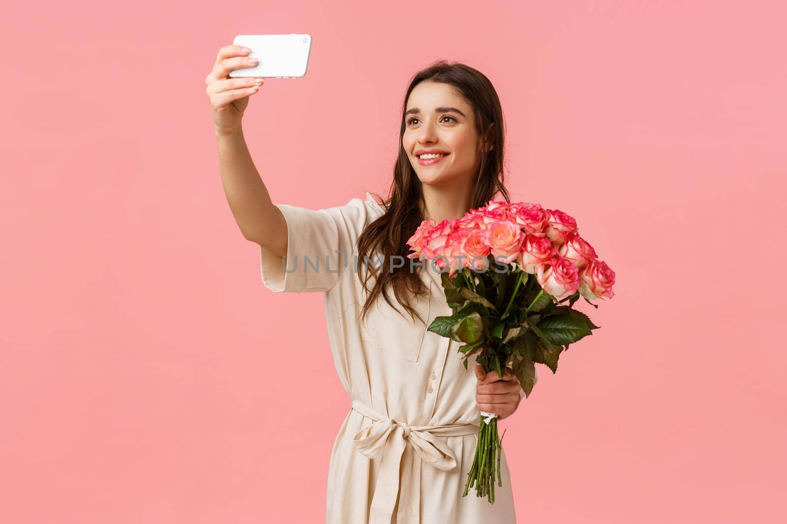 Birthday, holidays, romance concept. Charming alluring young caucasian woman receive delivery, got gift flowers, taking selfie on smartphone with beautiful bouquet, standing happy pink background.