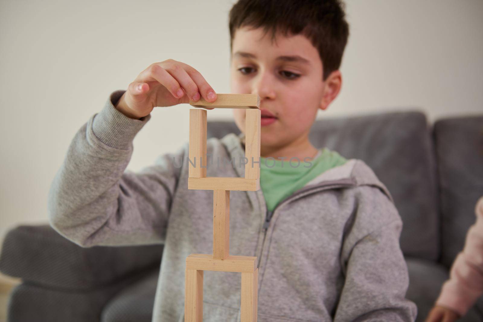 Close-up of the hand of European handsome puzzled schoolboy, concentrated on construction of complex tall structure from wooden blocks. Fine motor skills, concentration and educational leisure concept