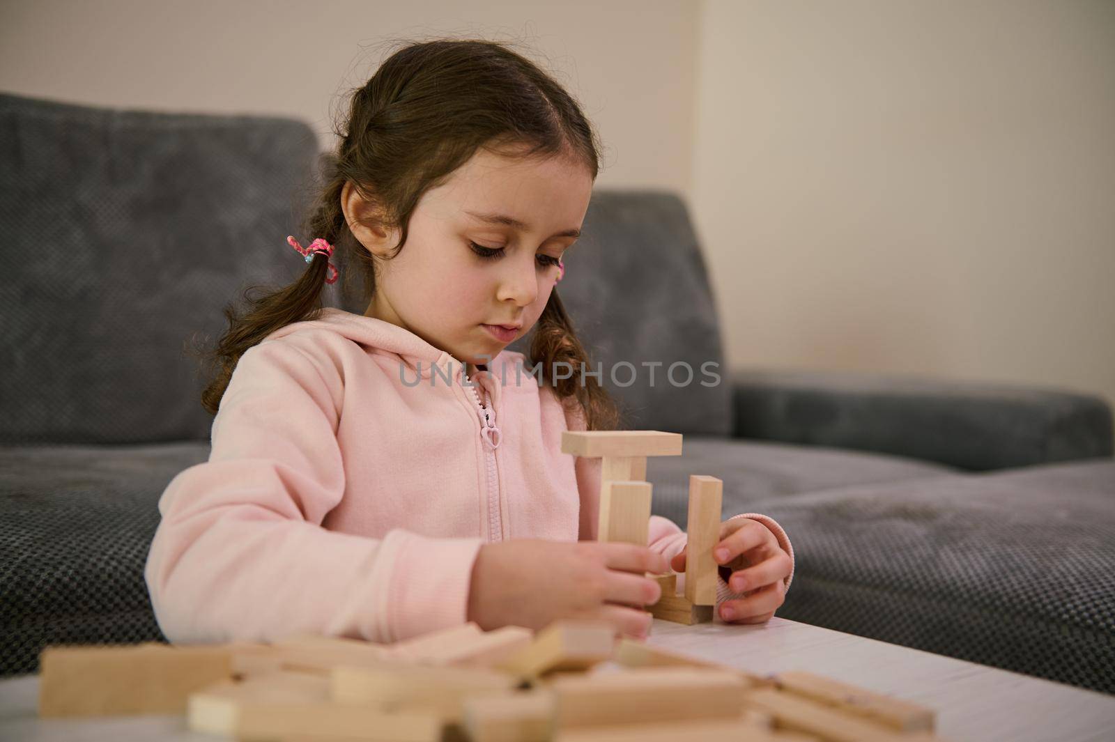 Cute adorable creative child European little girl playing board game, concentrated on building constructions with wooden blocks bricks. Hand movement control and building computational skills concept.