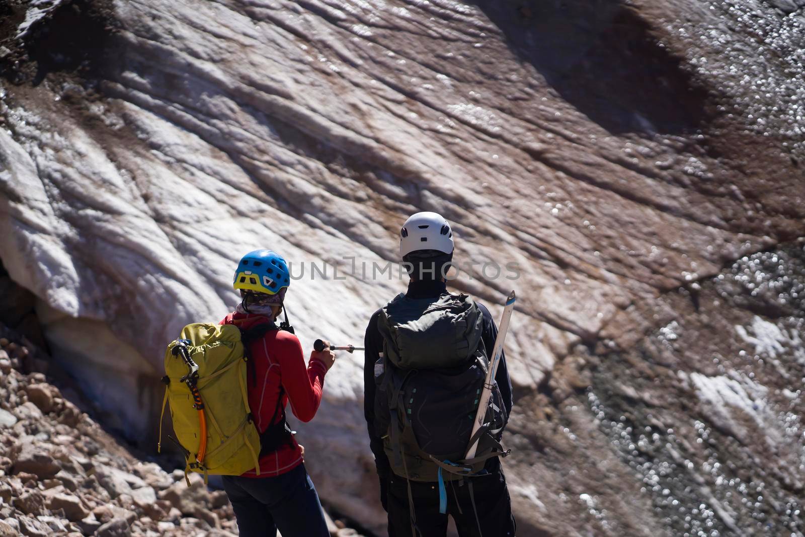 Two climbers discuss, plan a route to the summit and climb a glacier in the mountains with tourist equipment, people in helmets, with a rope and backpacks travel on rocky terrain.