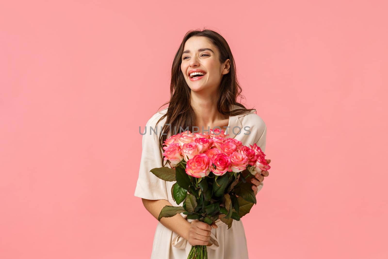 Valentines day, romance, celebration and beauty concept. Charming elegant and feminine young woman receive flowers, holding beautiful bouquet and laughing joyfully, pink background.