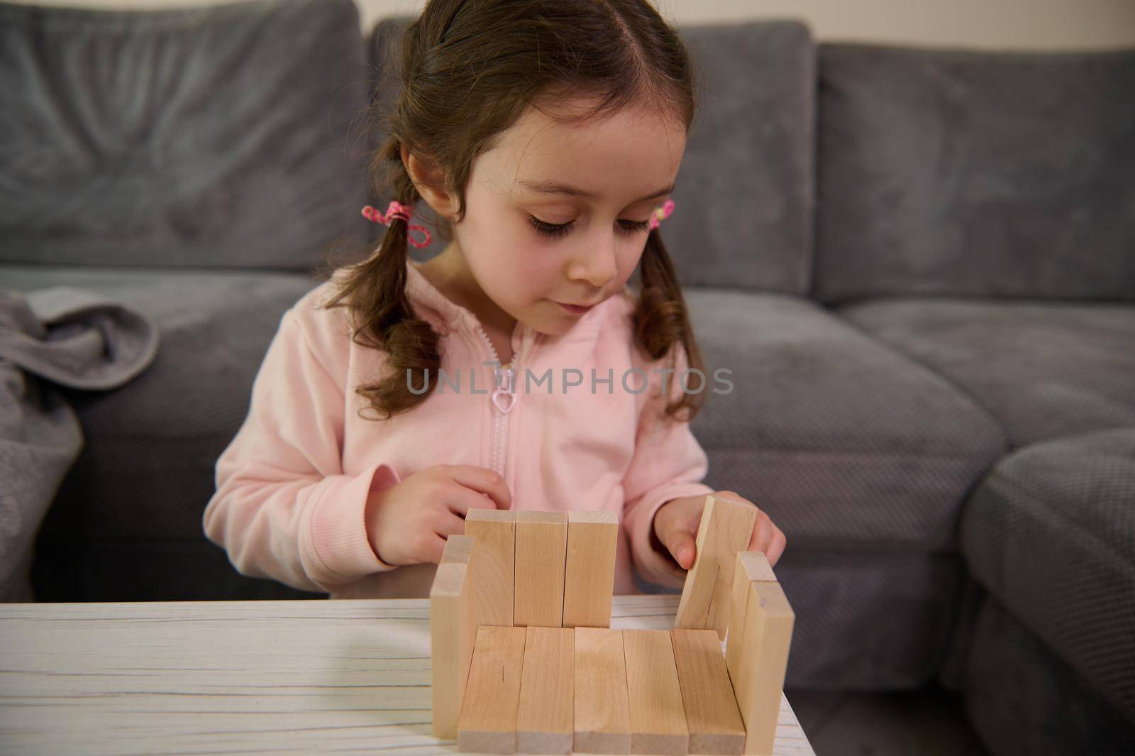 Adorable Caucasian 4 years old baby girl building house with wooden bricks and blocks. Hand movement control and concentration skills concept, educational board games by artgf