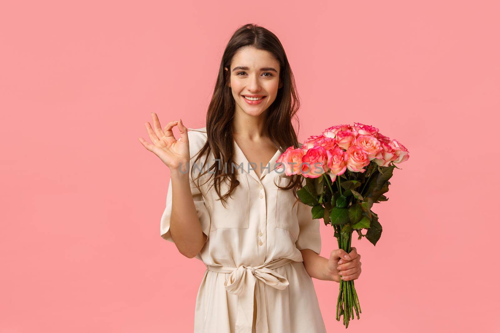 Best holiday ever. Cheerful lovely caucasian girlfriend in dress with curly stylish haircut, showing okay, approval gesture as holding beautiful bouquet roses and smiling, having great valentines day.