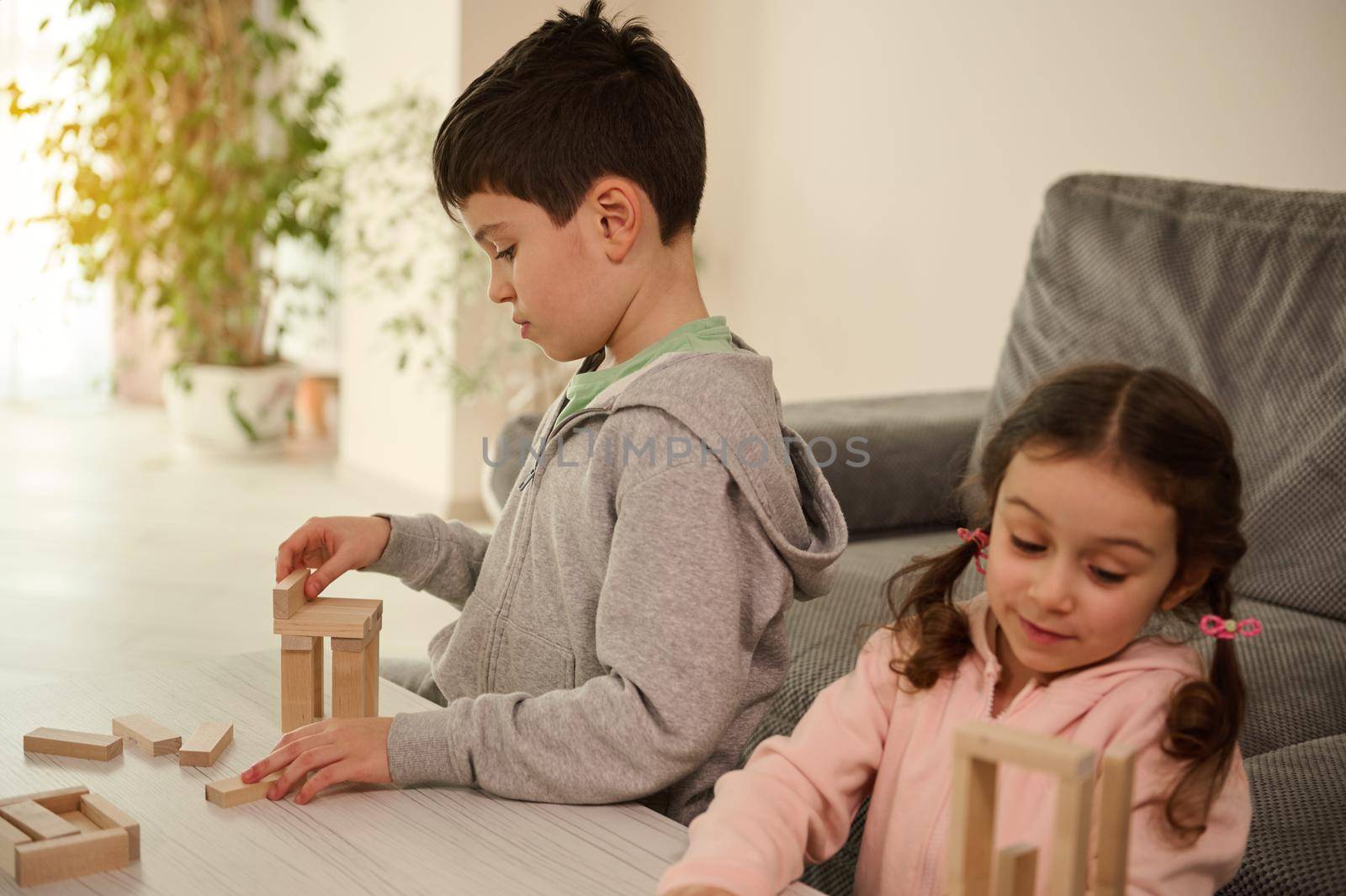 Focused children building structures with wooden blocks, playing board games in the home living room. Development of fine motors skills and concentration, educational leisure, family pastime concept.