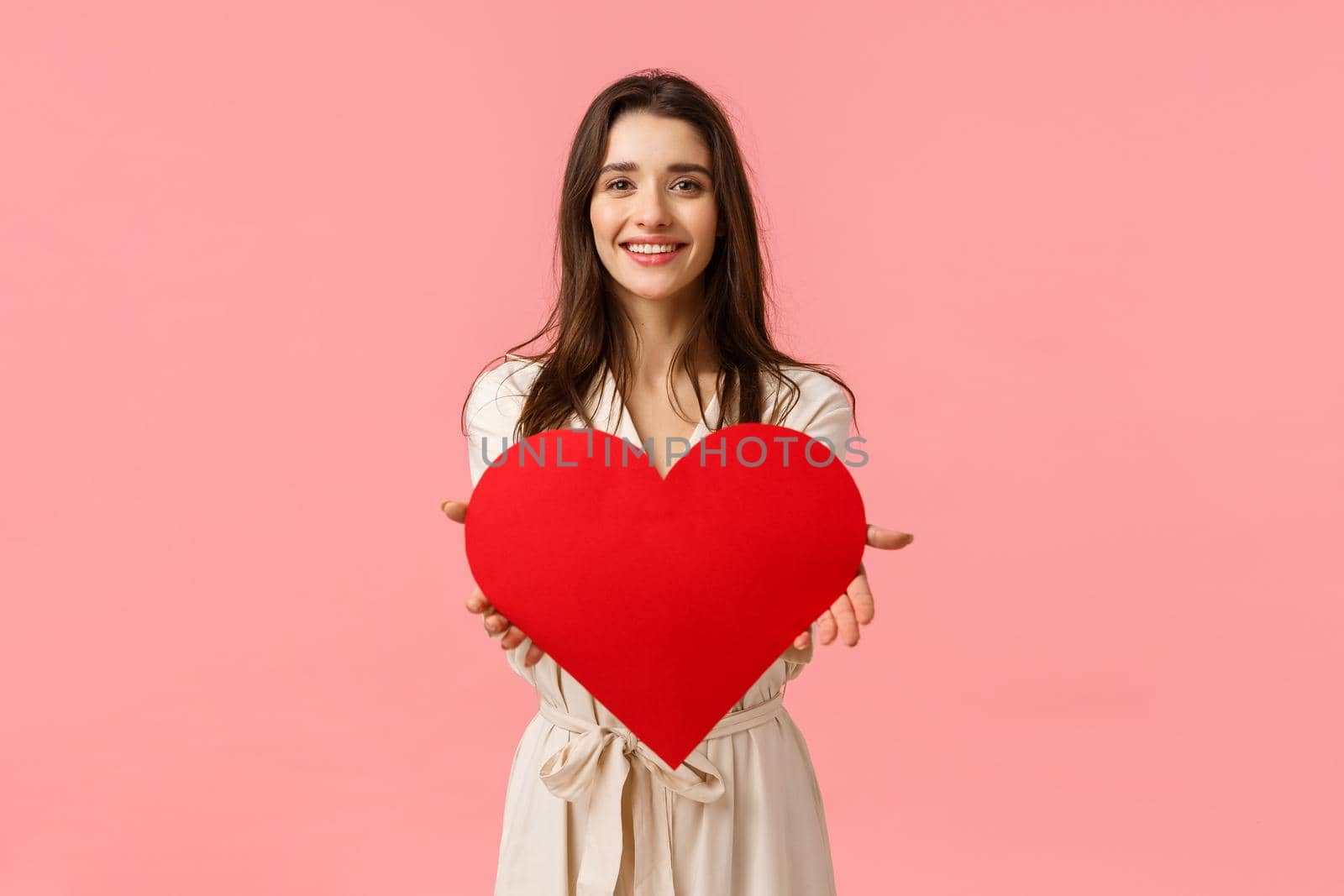 Here my love to you. Charming tender and alluring, romantic young woman giving big heart card to camera, smiling delighted, express her affection and admiration, standing pink background by Benzoix