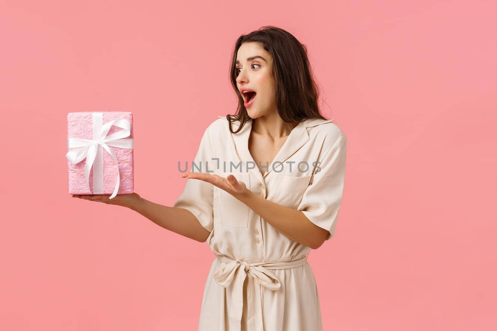 Girl likes surprises. Amused and happy cheerful young brunette woman in dress, receive gift box, pointing at present looking impressed and astonished as didnt expect such cuteness, pink background by Benzoix