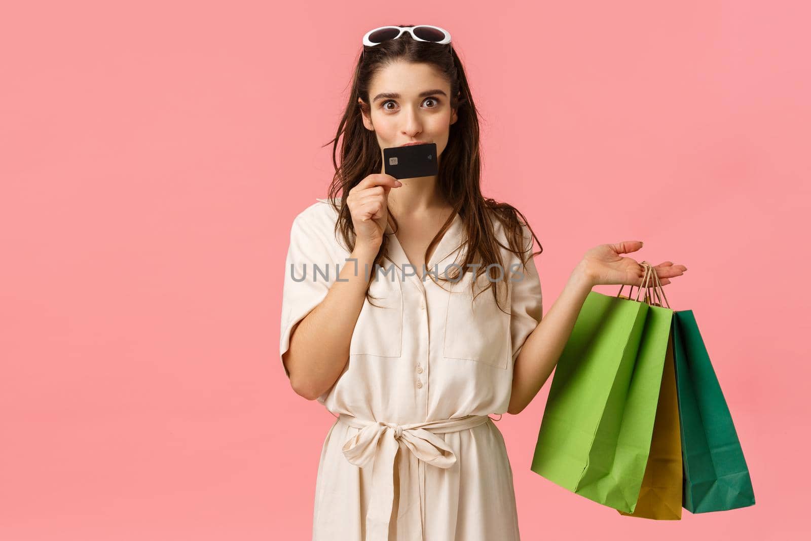Girl likes wasting money on her credit card, kissing it and smiling joyfully, carrying shopping bags, shop in stores, getting new clothes, prepare gifts for girlfriends, standing pink background.