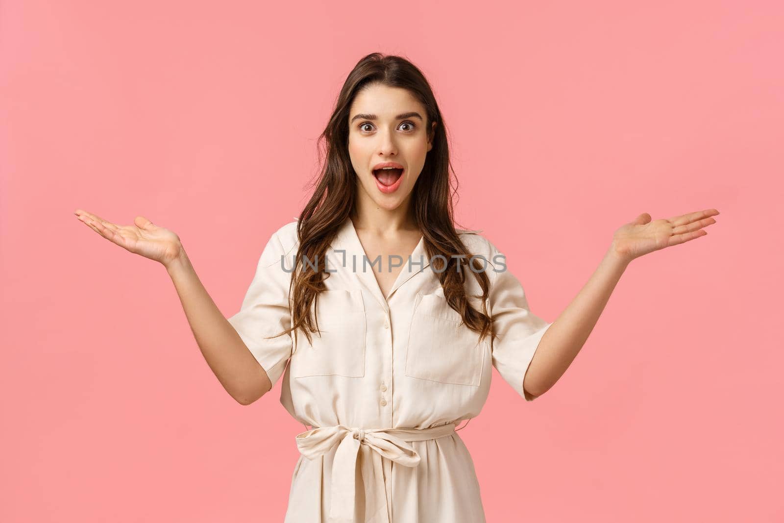 What a pleasant surprise. Amused happy glamour, gorgeous brunette female in cute dress, spread hands welcoming sideways, and smiling amazed, greeting friend, standing pink background.