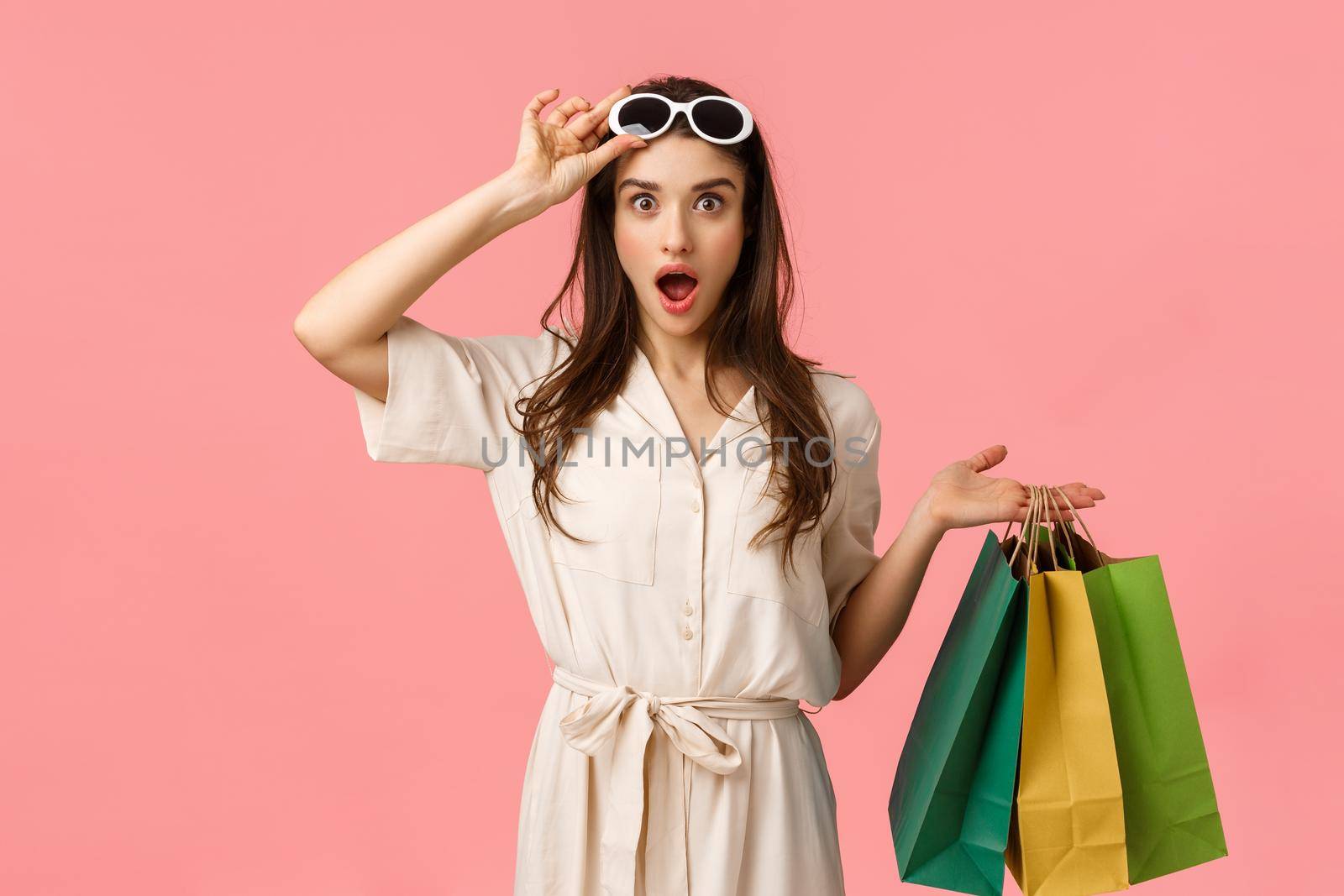 Lets go shopping. Amused and excited female shoppaholic having fun browsing through city malls, holding shop bags, taking-off glasses seeing exactly what been looking for, pink background.