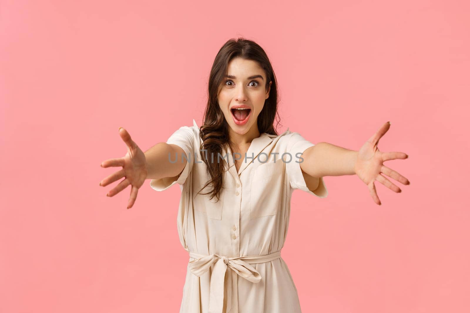 Come into my arms. Excited beautiful caucasian girl stretching hands forward to hold, take something, cheerfully smiling, embracing friend, greeting girlfriend, heading shopping, pink background.