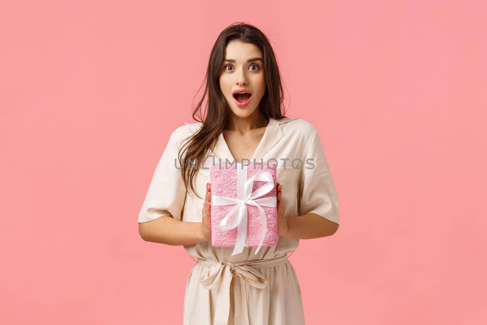 Celebration, happiness and emotions concept. Cheerful young woman receive pleasant gift, holding wrapped present, gasping amazed, open mouth and looked fascinated, pink background.