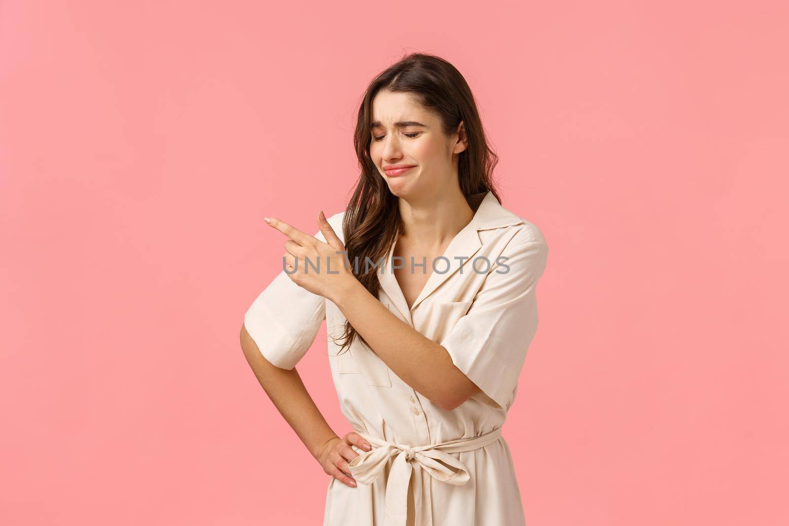 Upset silly brunette caucasian girl in dress, crying and sobbing pointing upper left corner, regret missed opportunity, feeling uneasy or heartbroken, standing pink background distressed.