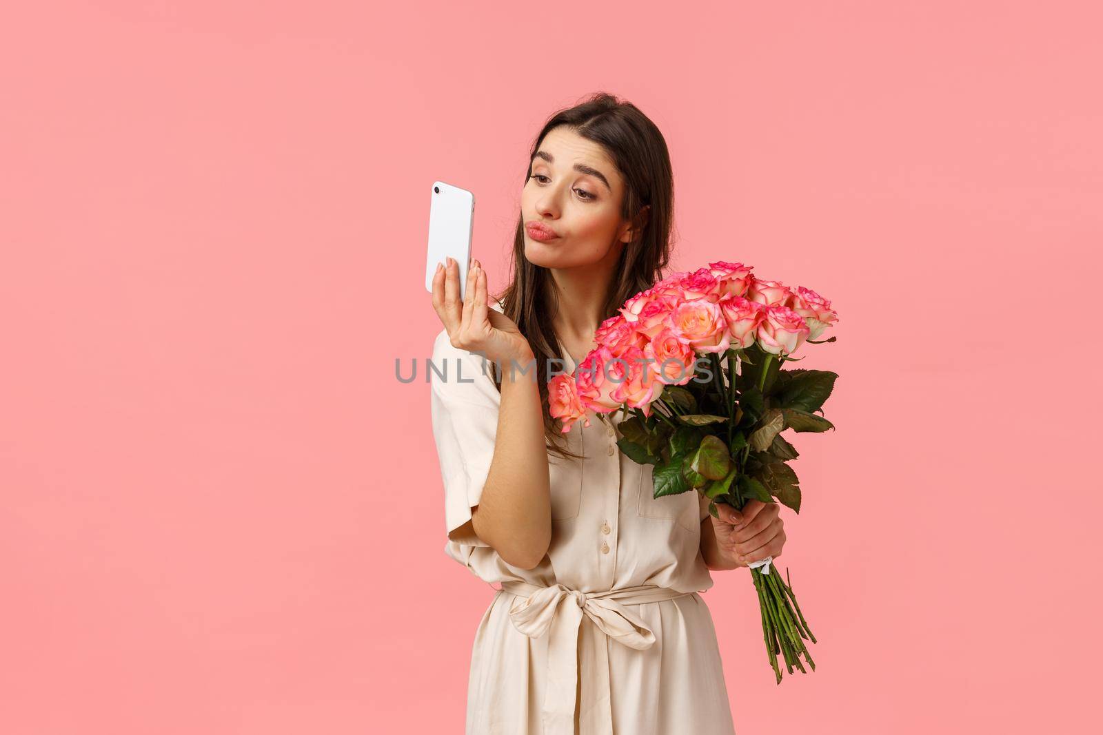 Romance, relationship and beauty concept. Tender and silly coquettish young b-day girl receiving bouquet want take selfie with flowers from secret admirer, checking lipstick on mobile camera.