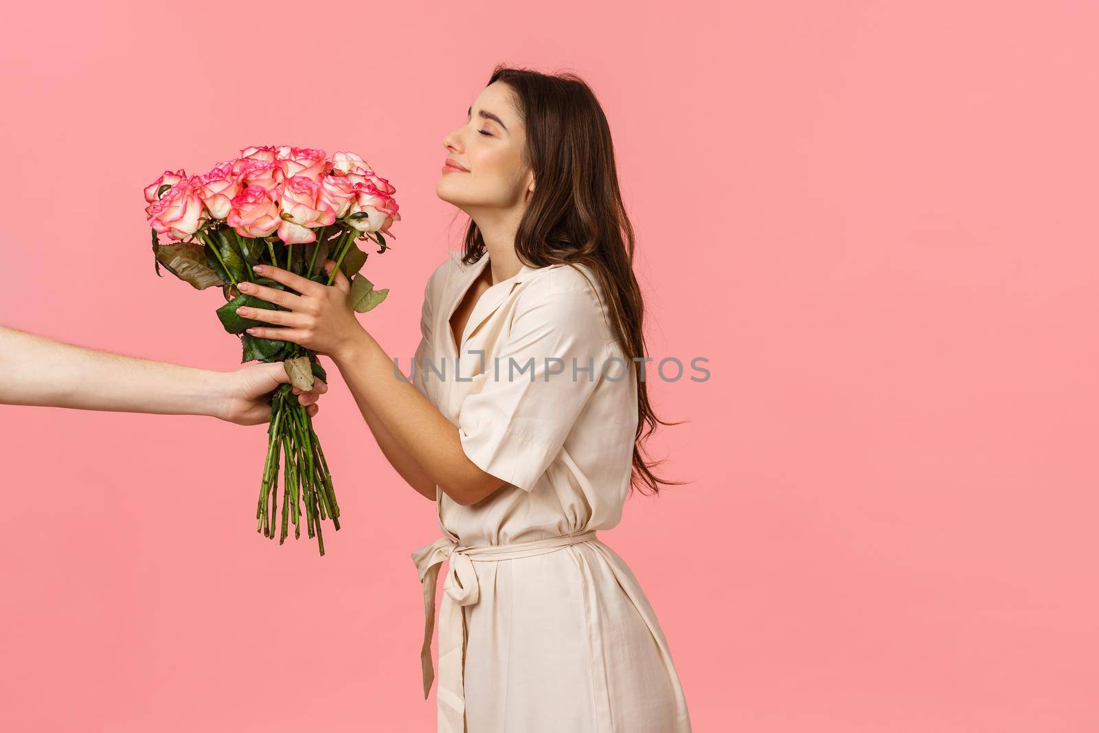 Romance, valentines day and happiness concept. Gorgeous young woman receiving delivery, smelling pretty roses as hand extending bouquet to girl, smiling delighted, got surprise gift, pink background.
