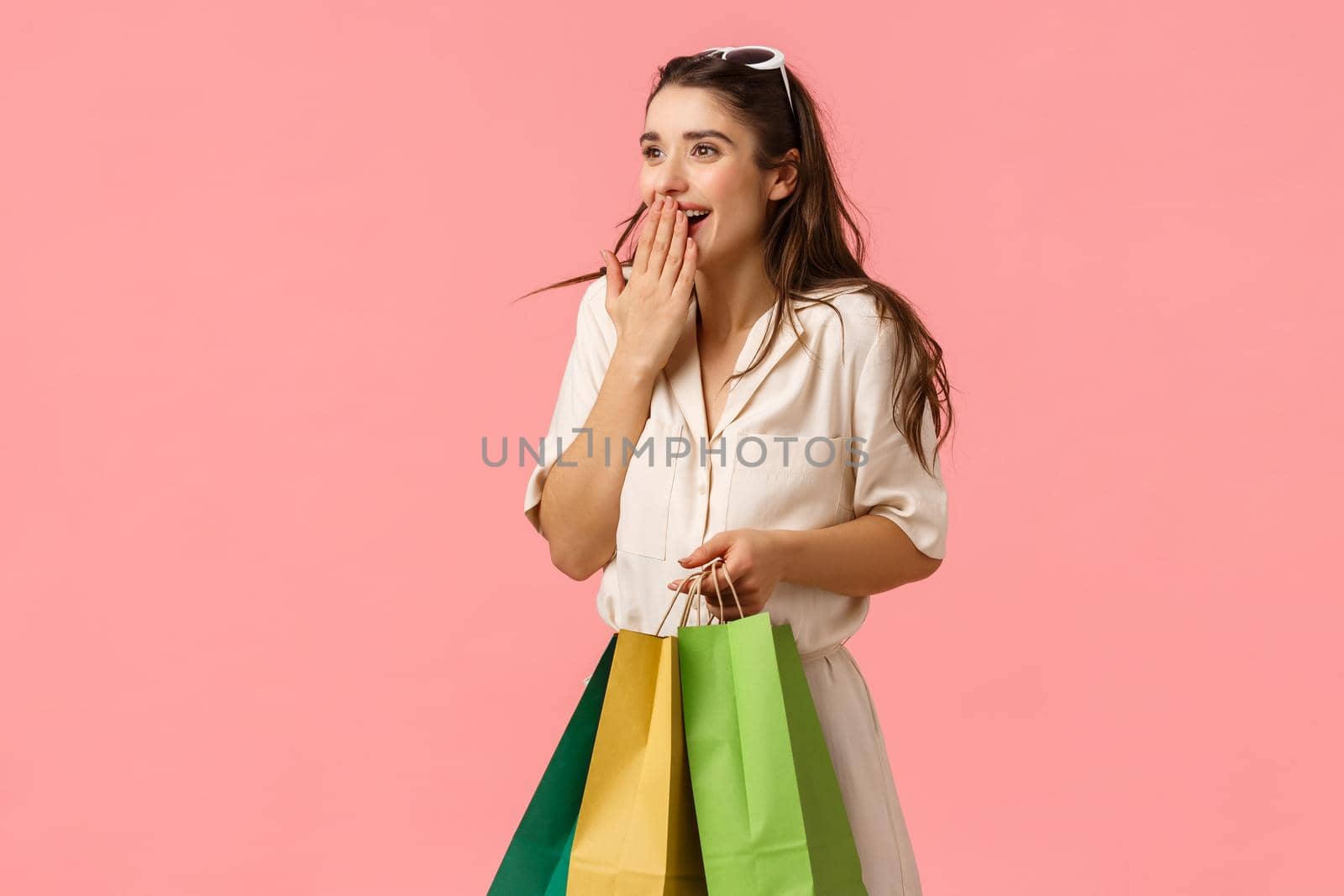 Excited and fascinated cute feminine brunette female in dress, holding shopping bags, wonder around mall, gasping excited cover mouth seeing something wonderful, pink background by Benzoix