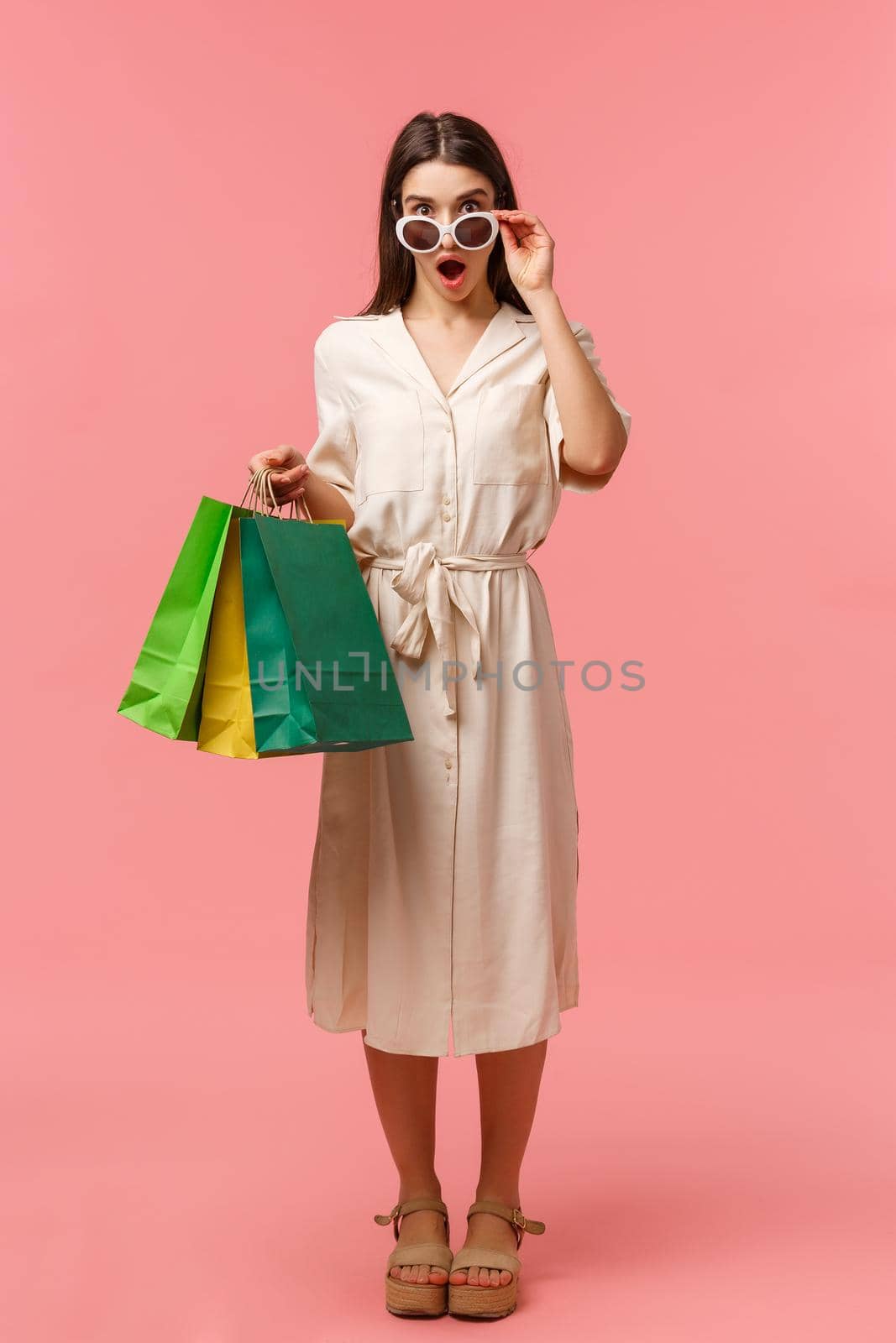 Full-length vertical portrait excited and speechless, amazed young brunette woman seeing something amazing and pretty, taking off glasses to look closer, open mouth fascinated, holding shopping bags by Benzoix