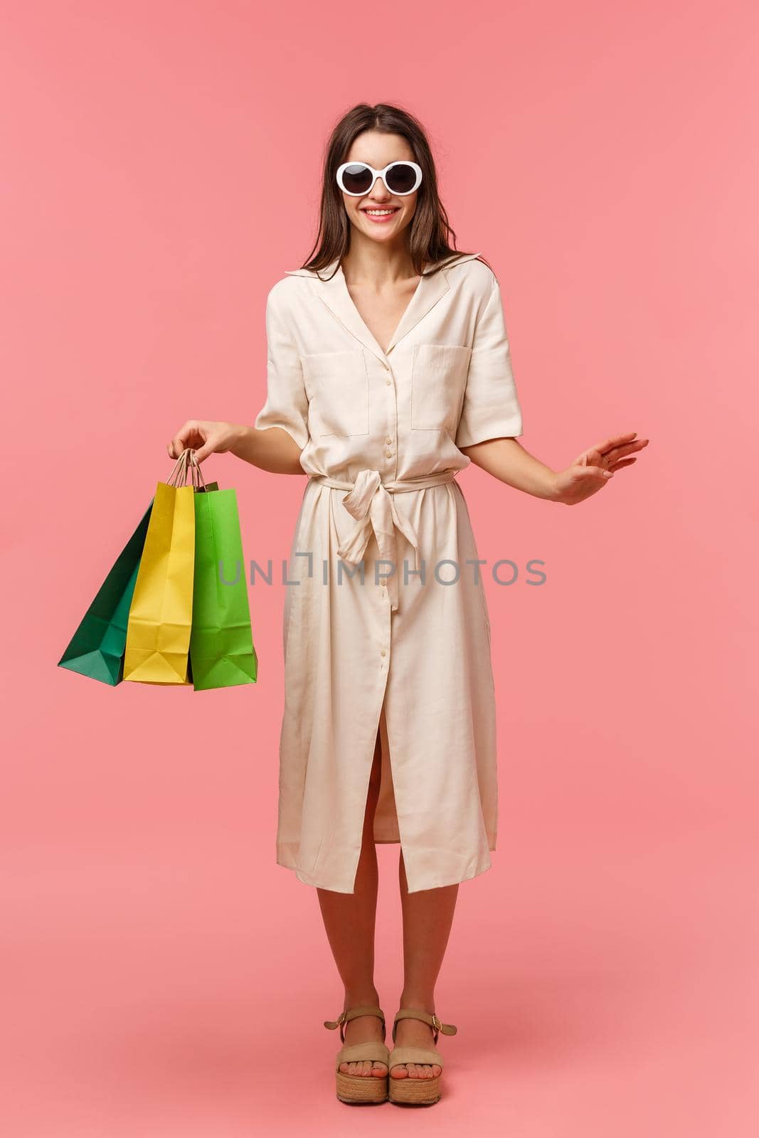 Full-length vertical portrait elegant good-looking woman on vacation, shopping and having fun in malls, wearing sunglasses, light dress, carry bags from store, standing pink background smiling by Benzoix