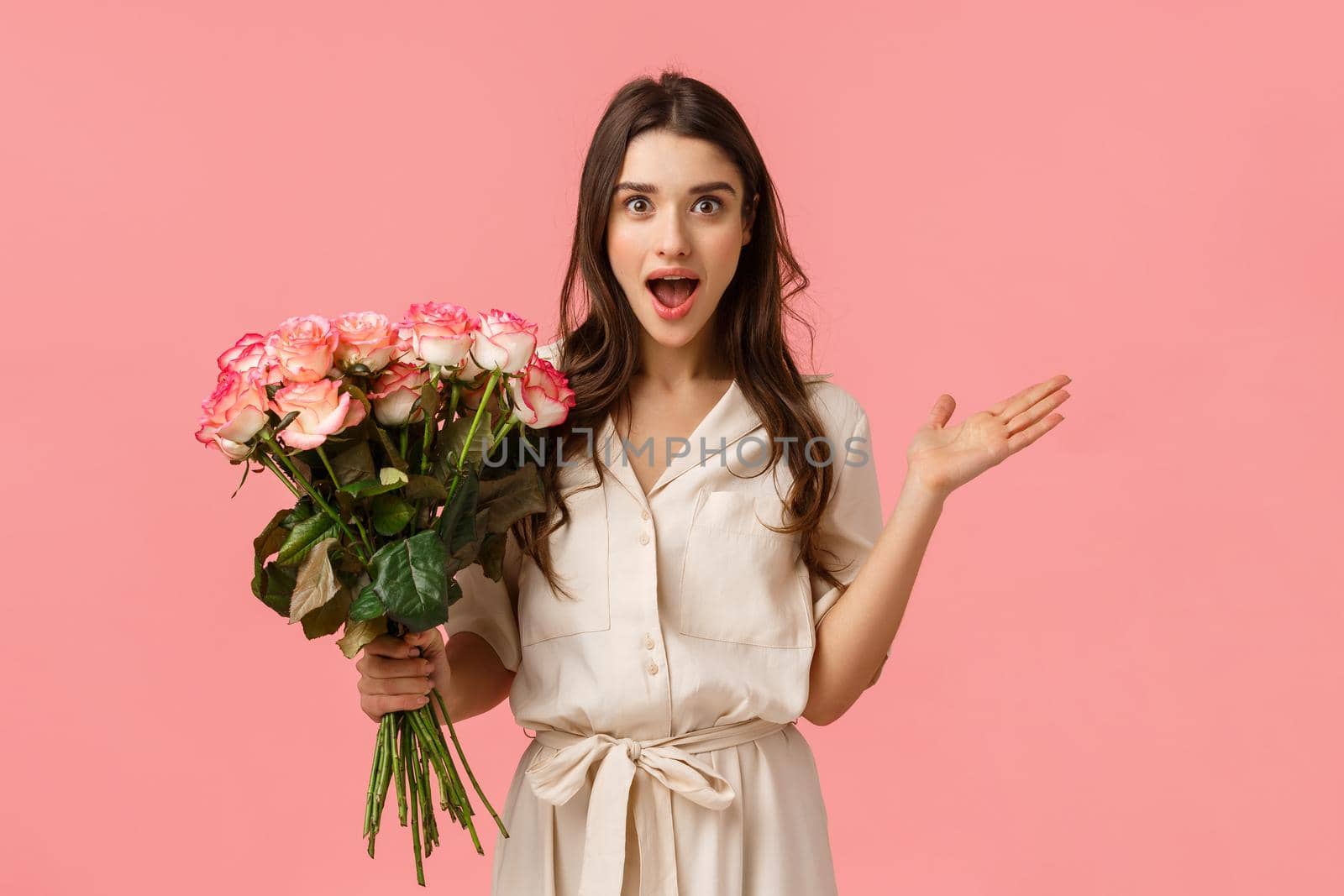 Excited and amused, surprised gorgeous modern woman in trendy dress, spread hands sideways amazed and astonished, look astounded by nice gesture, holding pretty flowers, roses bouquet.