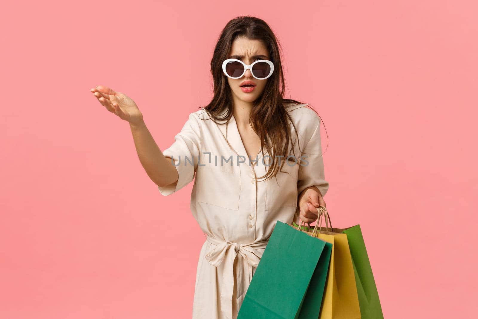 Thats total trash, wtf. Disappointed and bothered sassy glamour young shoppaholic, woman in dress holding shopping bags, pointing at something disgusting, show condemn or scorn by Benzoix